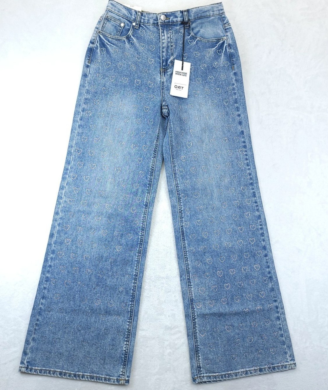 Oat Jeans high rise wide leg blue denim jeans with allover rhinestone heart print, laid flat on a white surface