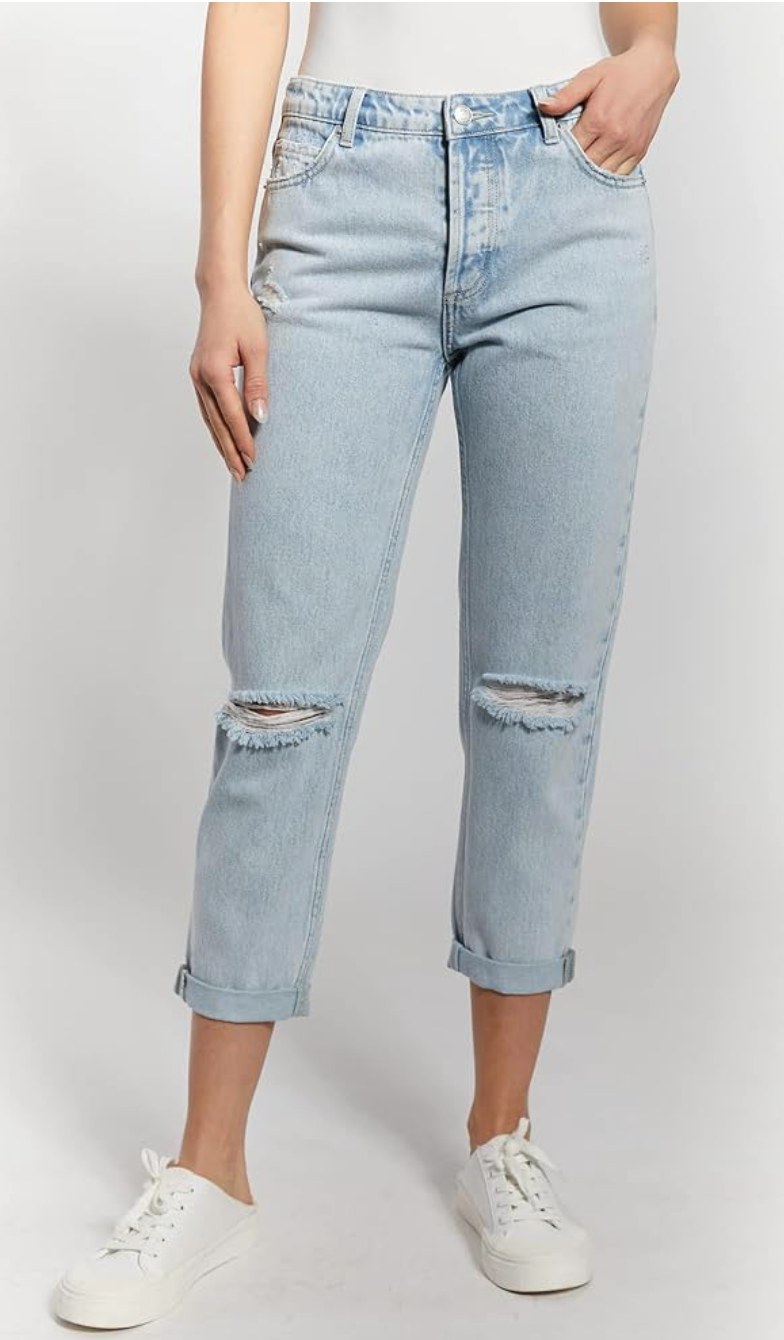 Woman wearing light blue wash distressed boyfriend crop jeans with ripped knees and rolled cuffs, styled with white sneakers